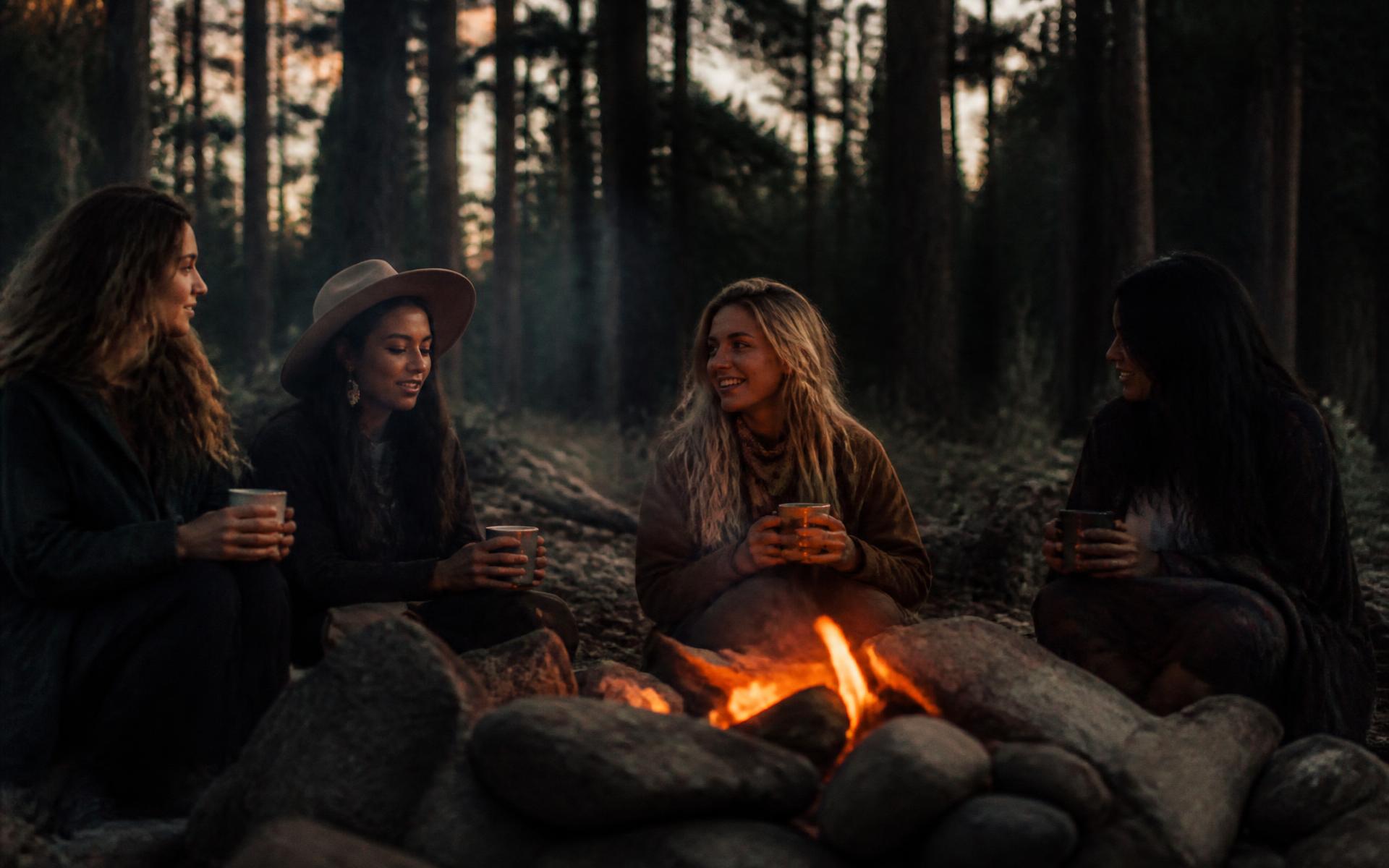 Mothers sitting together around a fire in a pine forest at dusk
